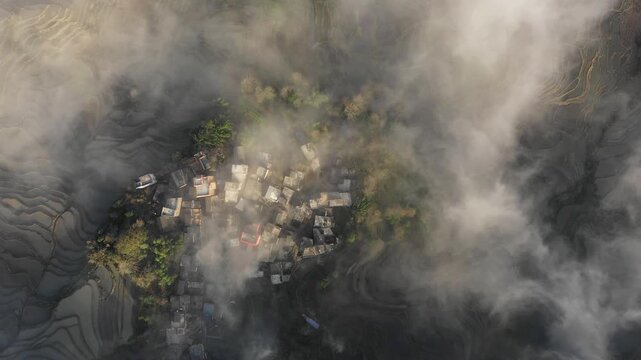 Overhead drone flight over cloud covered mountain village set in spectacular terraced rice fields in Yuanyang, Southern China
