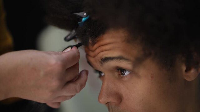 Professional hairdresser working on a client's afro hair. Close-up on the patient face of a mixed-race man getting dreadlocks extensions