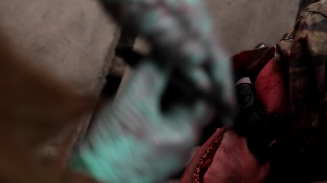 Close-up horizontal shot of a combat medic in bloody blue gloves looking at a tactical smartwatch to record the exact application time on a wounded soldier's tourniquet