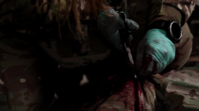 Close-up horizontal shot of a combat medic in blue gloves using trauma shears to cut through a camouflage uniform to access a bleeding wound for emergency treatment