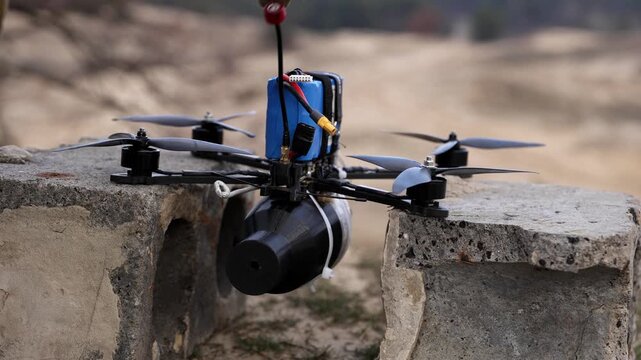 Horizontal shot of a soldier's gloved hand placing a tactical FPV drone with an explosive payload onto a concrete structure before takeoff.
