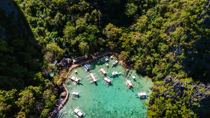 Aerial view of the iconic Kayangan Lake docking area in Coron, Palawan. Traditional bangka boats anchored in crystal clear turquoise water surrounded by majestic limestone karst cliffs © Michele