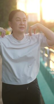 Middle-aged Asian woman stretching her shoulders and arms before morning exercise at the park.