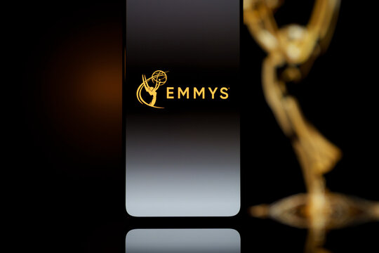 Emmys logo displayed on a smartphone screen with a blurred gold award statuette in the background, television industry awards and digital streaming concept