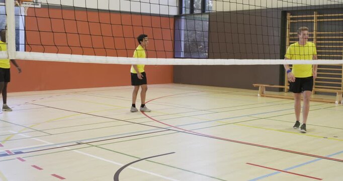 Diverse men team in yellow shirts gym setter sending volleyball over net blue-shirt spiking aiming