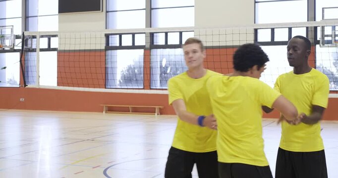 Six male players in jerseys exchanging handshakes after meeting at net joining gym pep huddle
