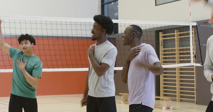 Diverse male players after green-shirt signal doing chest taps rotating at volleyball net warming