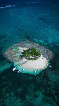 Aerial view of a small tropical island with palm trees, white sand beach, and traditional outrigger boats in turquoise water in