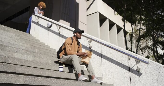 Diverse strangers, African American man sitting on skateboard opening paper bag and taking snack