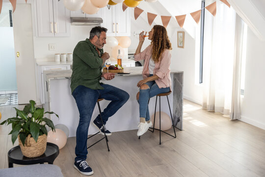 Couple sitting on bar stools at marble kitchen island celebrating with wine and charcuterie board