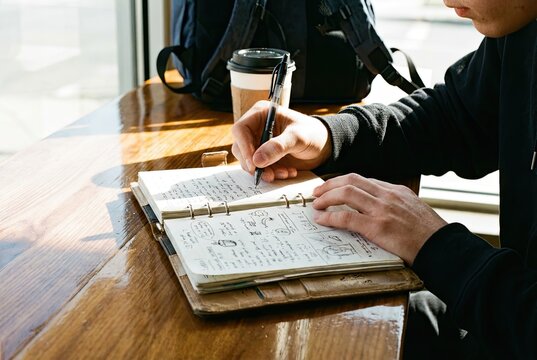 Hands Writing in Planner with Pen on Polished Surface