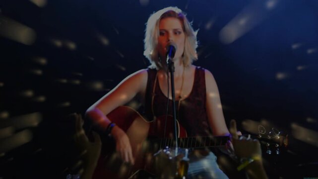 Music performer strumming guitar and singing while camera focusing, lights sweeping, engaging fans