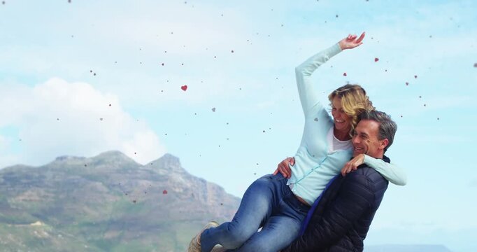 Vertical video: Lifting man holding woman on sea cliff, confetti drifting, blue sweater, copy space