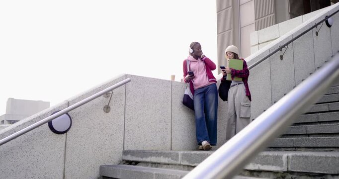 Diverse female pals on stairs greeting arrival checking phones green folder taking selfie