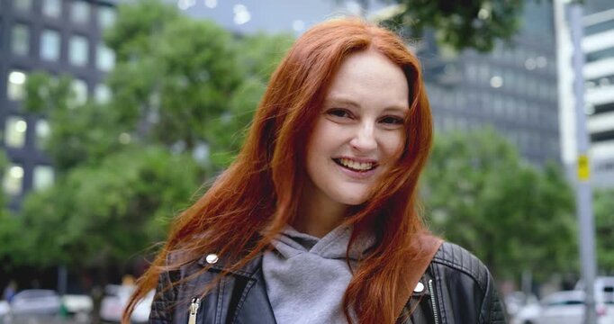 Adult woman smiling laughing tucking hair from wind fixing bag on city street in leather jacket