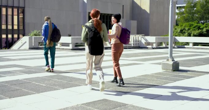 Diverse female friends walking on campus, beanie woman calling newcomer to join, notebooks visible