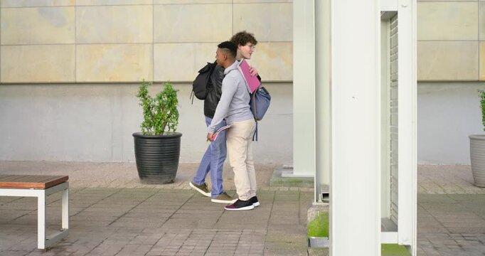 Diverse male friends walking plaza stopping as other appearing, swapping red folder for class notes