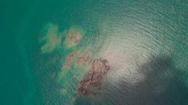 A drone looks down on a turquoise sea with rocky coral formations creating patterns beneath the clear water.