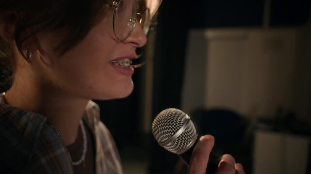 Extreme close up of young female stand up comedian with braces delivering jokes into mic performing on low key lit stage of comedy venue, copy space