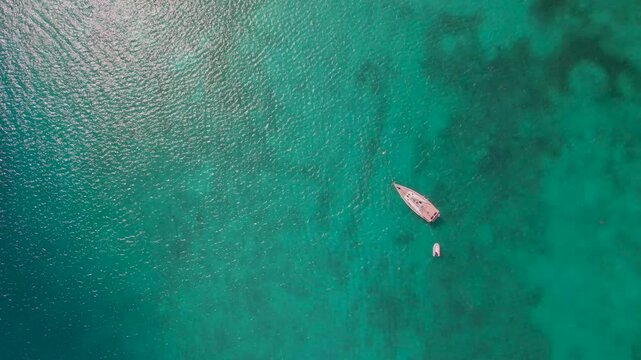 Aerial view of a small boat and dinghy floating on clear turquoise water in the Caribbean.
