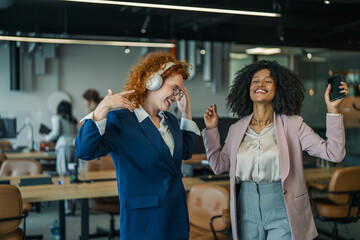 Naklejka premium Diverse businesswomen celebrating success and dancing in modern office