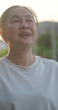 Middle aged Asian woman closing eyes and breathing fresh air in the park at sunset.