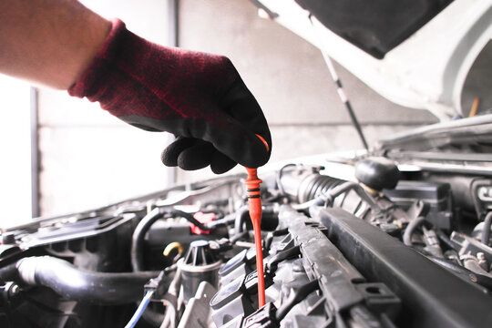 Car Engine Oil Dipstick Check, A gloved hand pulls the orange engine oil dipstick to check fluid levels and quality during a routine vehicle maintenance inspection.