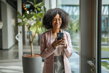 Smiling businesswoman checking smart phone in modern office building