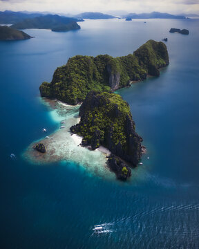 Aerial view of the lush tropical landscape and limestone cliffs of Miniloc Island surrounded by turquoise water and small boats