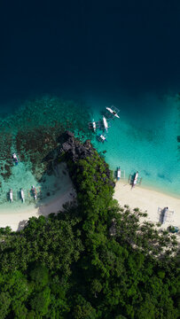 Aerial view of traditional outrigger boats anchored in turquoise waters along a white sand beach lined with palm trees El Nido,