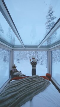 Enjoying a warm drink while surrounded by mesmerizing snowy landscapes, two friends relax in a modern glass cabin in Akaslompolo, Lapland, Finland, embracing the winter magic.