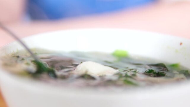 Stirring miso soup with spoon seaweed tofu egg in white bowl Asian cuisine healthy warm meal close-up