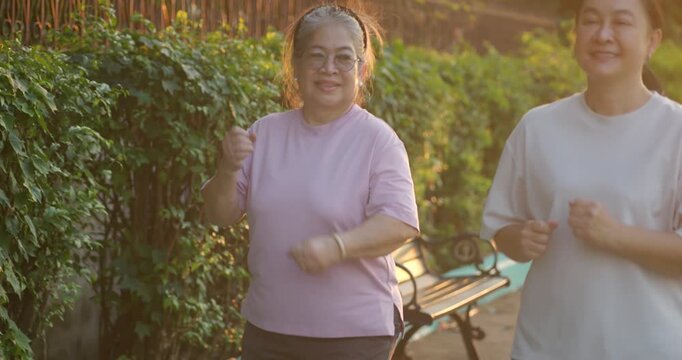 Two Asian women jogging and exercising together in the park during sunset.