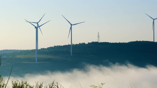 Wind farm generators work with renewable power source on hazy mountain. Windmills produce electricity at highland station slow motion