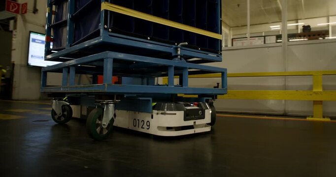 Autonomous mobile robot transporting a heavy blue cargo rack through a large industrial warehouse facility