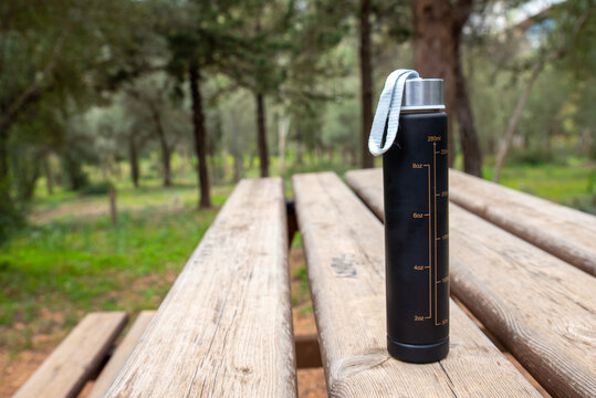 reusable water bottle with measurement markinkgs 280 ml on a wooden table in a park,hydration and healthy lifestyle concept