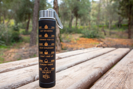 reusable water bottle with measurement markinkgs 280 ml on a wooden table in a park,hydration and healthy lifestyle concept