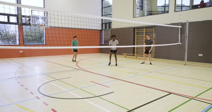 Diverse male team preparing, server rolling purple volleyball, setter jumping to set in school gym