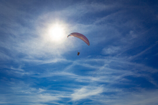 Paraglider flying over a blue sky in front of the sun.