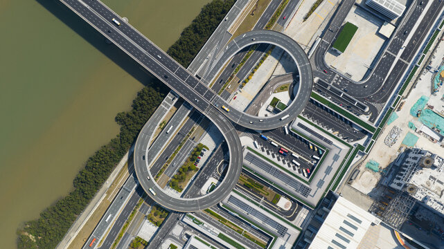 Aerial view of a highway bridge shaped like an infinity loop over a river, amidst the contrasting textures of water and concrete, Zhuhai, China.