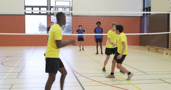 Diverse male players in yellow reacting to return, digging at net to score, cheering at school