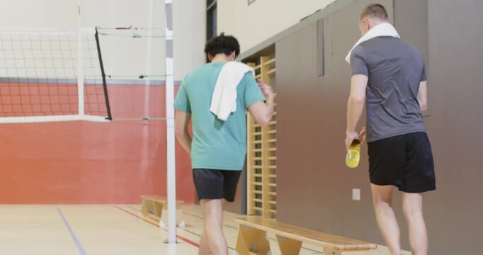 Male volleyball team walking on marked gym floor, arriving with ball and duffel, gathering for play
