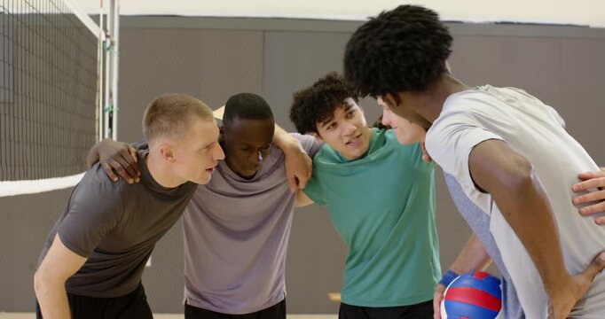 Diverse male team huddling in gym after rest, leader holding ball, stacking, planning then moving