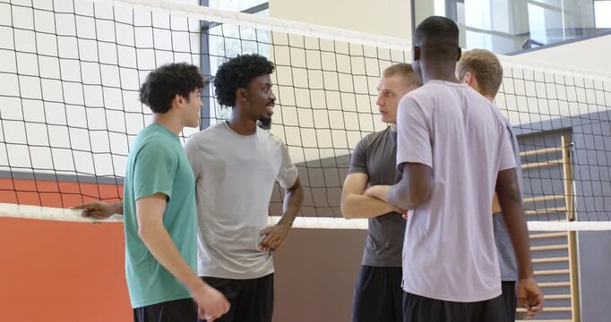 Diverse male teammates in sportswear holding volleyball and discussing strategy at gym net