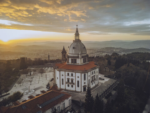 Aerial view of the Santuario de Nossa Senhora do Sameiro basks in the warm glow of sunset, its white facade contrasting with the red-tiled roofs, Braga, Braga, Portugal.