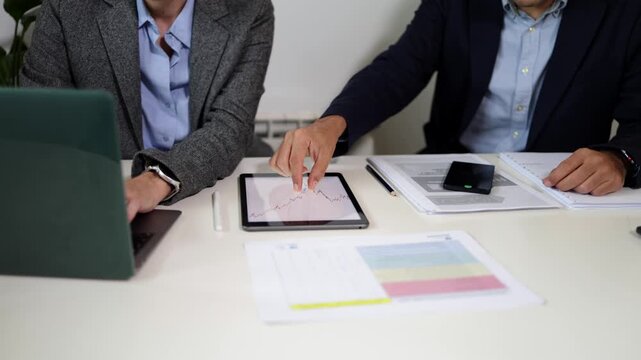 Frustrated businessman analyzing a declining stock market graph on a tablet during a corporate meeting with his colleague, showing anger and punching the table