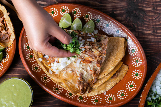 Close-up of a hand adding cilantro to a delicious gringa al pastor on a decorated plate
