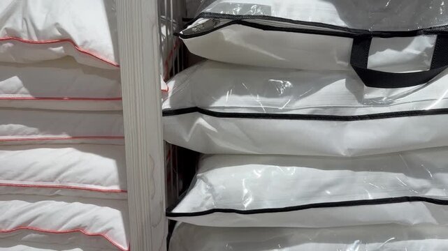 Fresh new white pillows for sleeping stacked high on shelves in a retail home goods store, showcasing a wide selection of bedding options and comfortable sleep accessories for sale