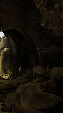 A dark cave filled with large rocks and boulders. In the distance, an opening lets in light. The scene appears to be set during twilight, creating shadows and depth in the cave.