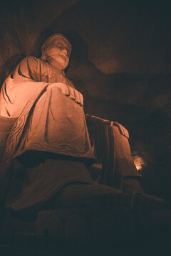 Serene Stone Buddha Statue in Leshan's Eastern Buddha Capital, Illuminated in Warm Light Within Cave Temple